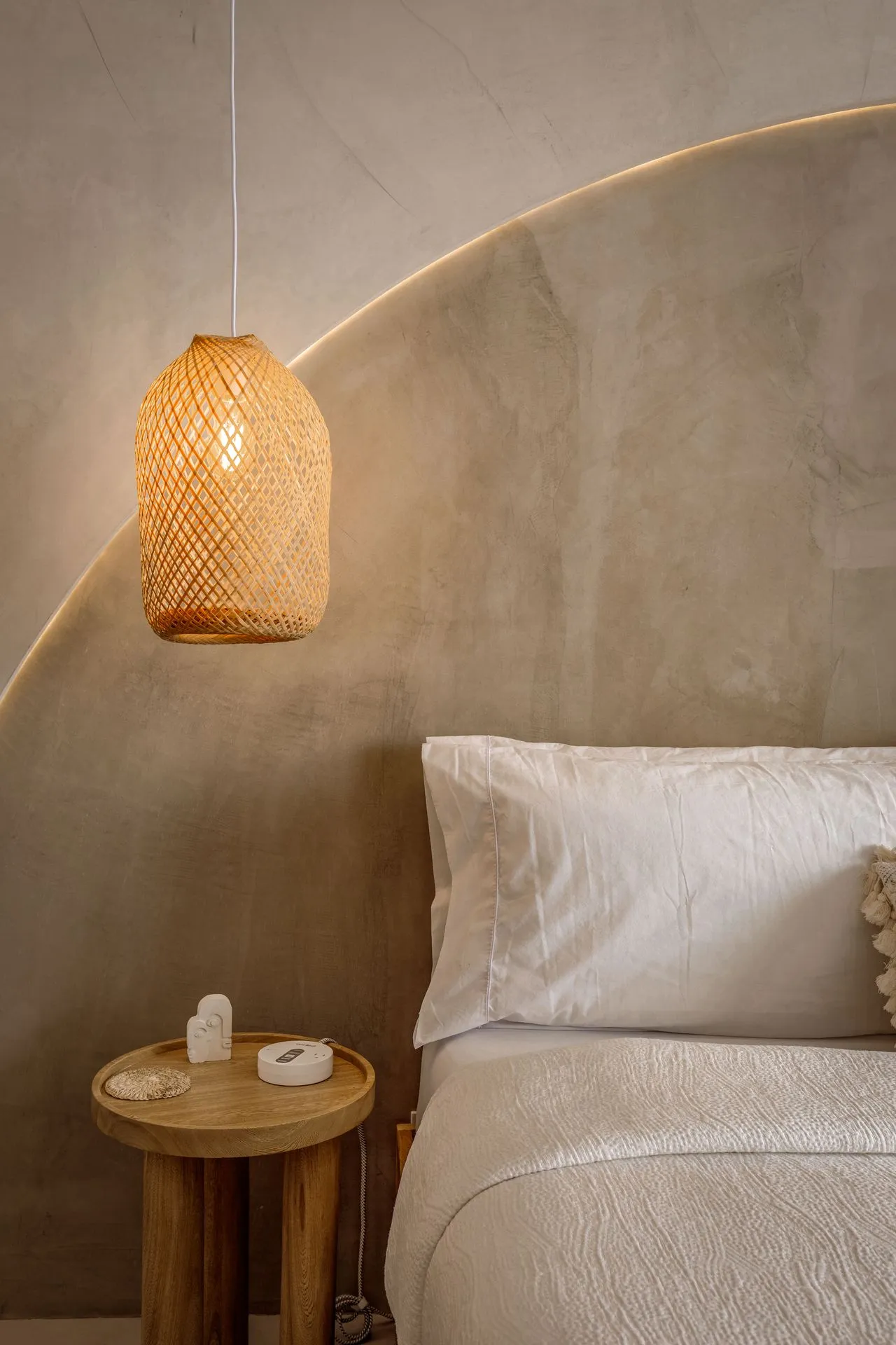 Calm bedroom with a woven pendant lamp glowing over white bedding and a small round wooden nightstand