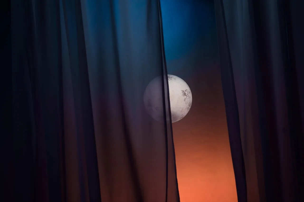 Dark curtains parted by a narrow gap showing a full moon at dusk