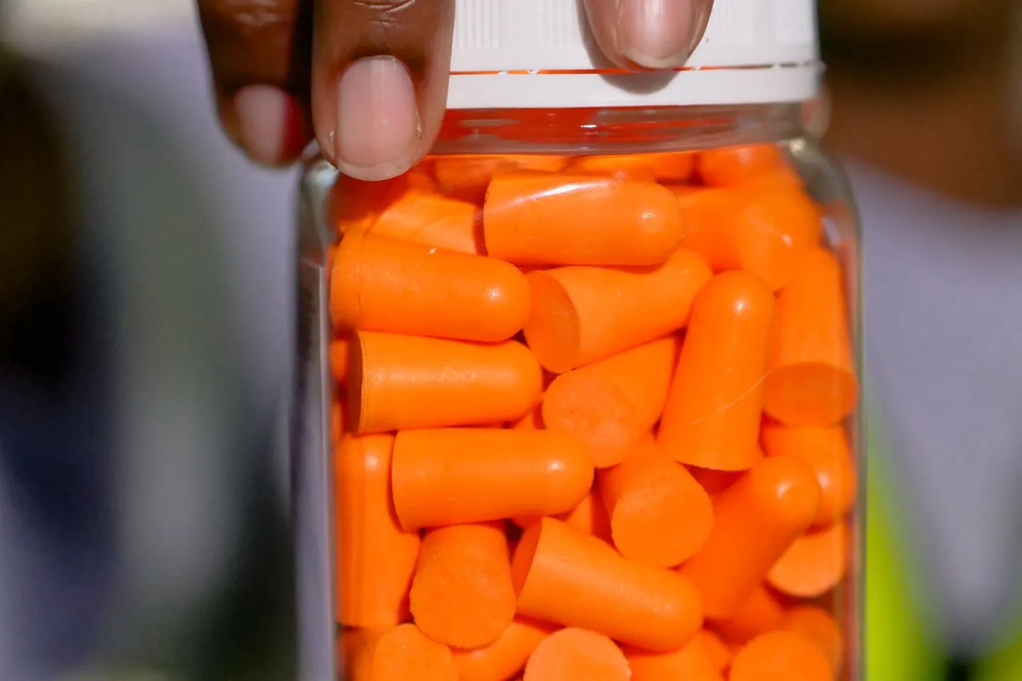 Orange foam earplugs filling a clear glass jar held up by a hand