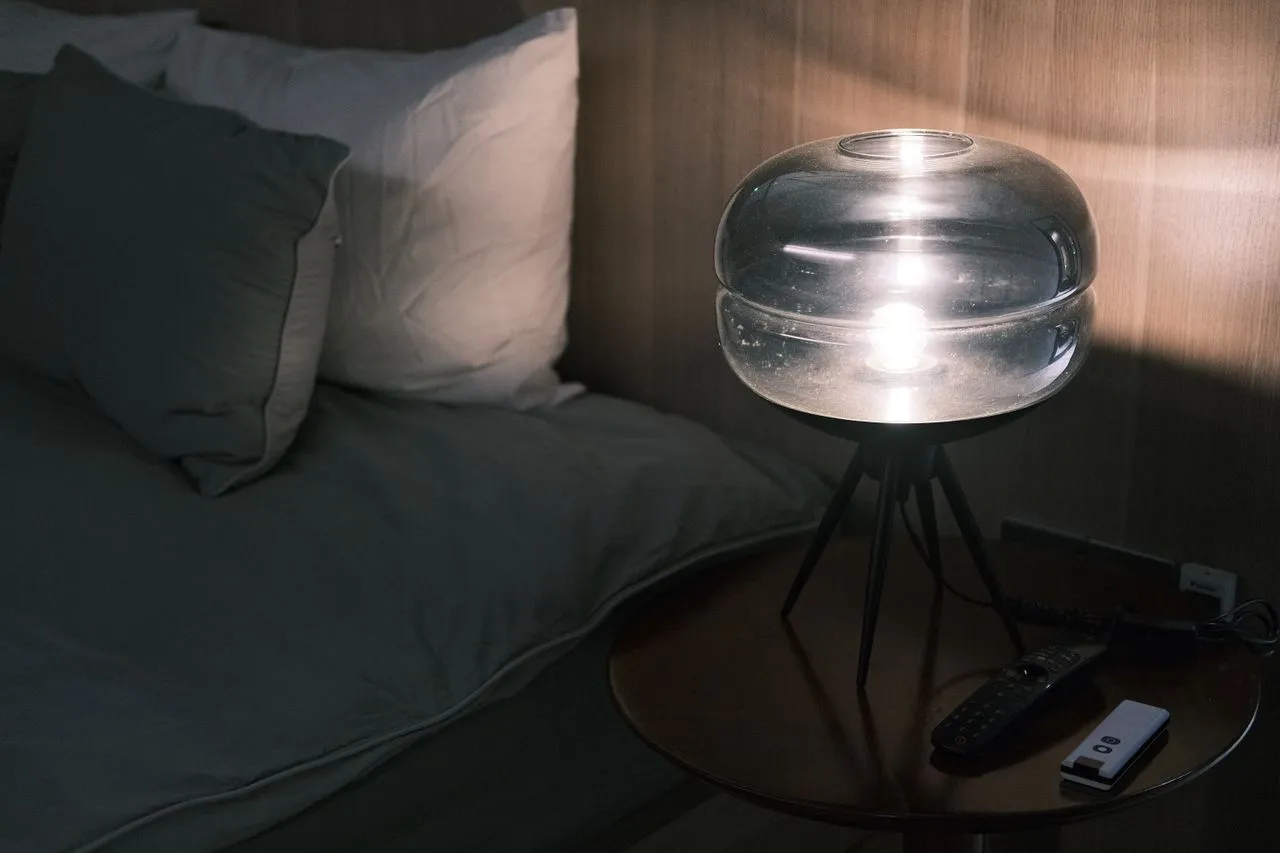 Round glass lamp glowing softly on a bedside table in a dark bedroom