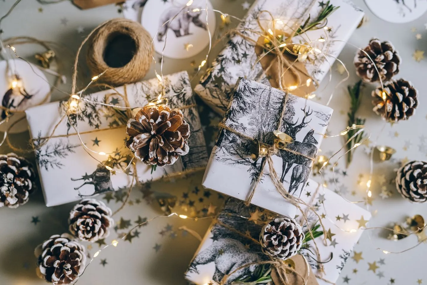 Gifts wrapped in white paper and twine with pine cones and warm fairy lights