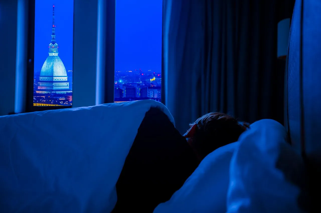 Dark bedroom at night with a city skyline glowing blue through the window