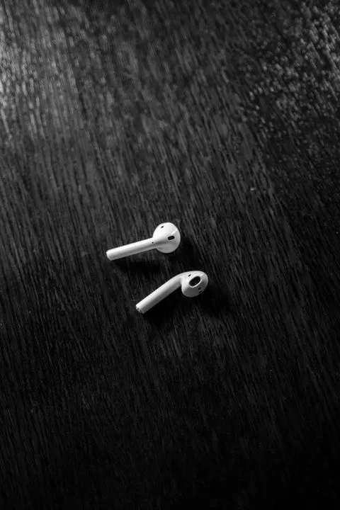 A pair of white wireless earbuds on a dark wooden table