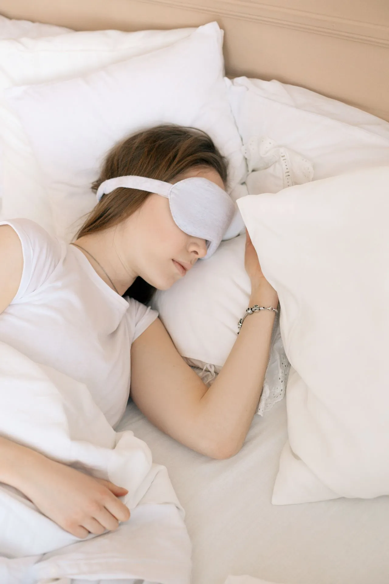 Woman asleep on white pillows wearing a pale satin eye mask