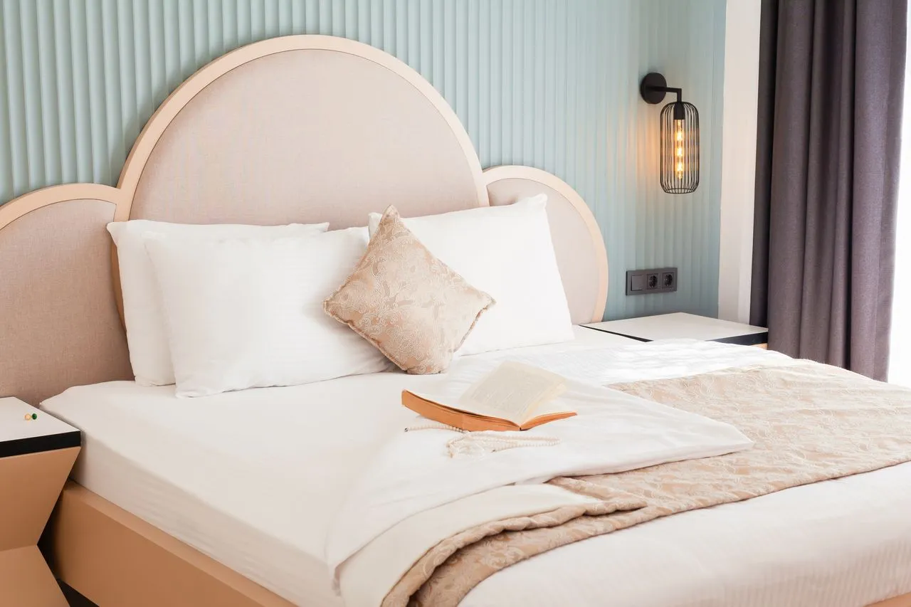 Made bed with white pillows and an open book under a soft arched headboard